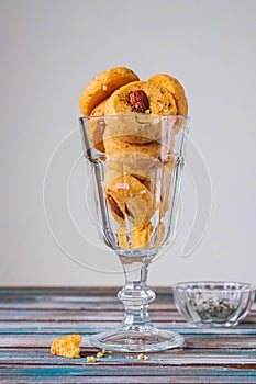 Unsweetened round cheese cookies with herbs and fried almonds in a glass glass on a wooden background. Savory cookie recipes as