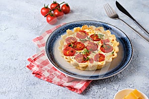 Unsweetened shortbread tartlets with feta cheese, cherry tomatoes and herbs on a blue plate on a light concrete background