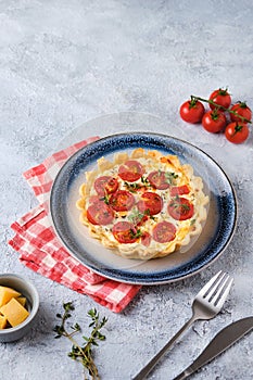 Unsweetened shortbread tartlets with feta cheese, cherry tomatoes and herbs on a blue plate on a light concrete background