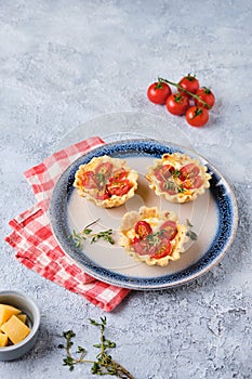 Unsweetened shortbread tartlets with feta cheese, cherry tomatoes and herbs on a blue plate on a light concrete background