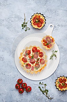 Unsweetened shortbread tartlets with feta cheese, cherry tomatoes and herbs on a white plate on a light concrete background.