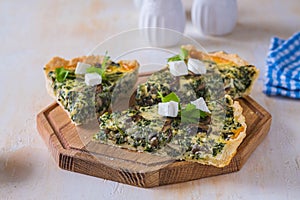 Unsweetened sliced open pie, shortcrust pastry quiche stuffed with spinach, mushrooms and cheese on a wooden board on a light