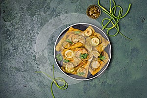 Unsweetened yeast pie with zucchini, pesto sauce and garlic arrows on a black plate on a green concrete background. Recipes for
