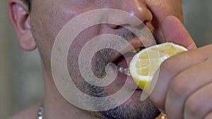 Untidy, unshaven man bites a slice of lemon, and juice flows from his mouth