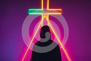 Man obscured by neon cross. A person stands holding a glowing neon cross in front of their face photo