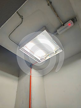 Fluorescent Ceiling Light with Exposed Electrical Wiring in Indoor Space.