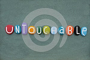 Untouchable word composed with multi colored stone letters over green sand