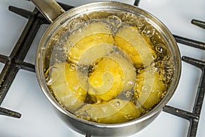 Untreated potatoes boil in a pot on a gas stove.