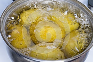 Untreated potatoes boil in a pot on a gas stove.