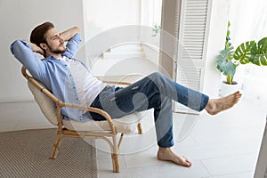 Untroubled millennial single man relaxing on chair in fashionable home photo