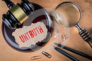 UNTRUTH. Law, regulations and judgment concept. Judge`s hammer, stationery and magnifying glass