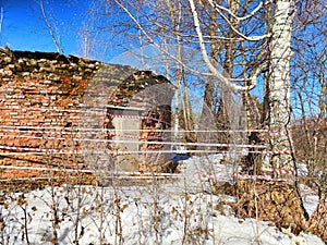 Unused brick structure in a snowy forest, surrounded by trees and caution tape in bright daylight photo