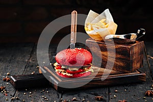 Unusual bright red burger with a knife and fries, on a wooden stand