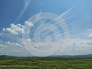 Unusual clouds float across the blue sky over the expanses of a hilly meadow.