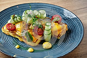 Unusual dish. Unsweetened waffles with herbs, tomato, cucumber and sauce on a beautiful blue plate.