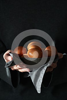 Unusual Easter on a dark background. A bowl of brown eggs with hands