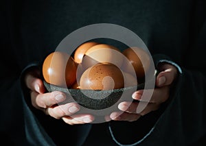 Unusual Easter on dark background. Bowl of brown eggs with hands