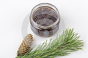 Unusual jam from pine cones in glass jar on white background among pine branches and cones. Organic and vegetarian sweet dessert