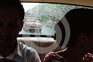 Unusual look on retro red car through rainy window and newlyweds