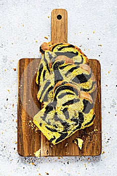 Unusual pumpkin marbled tiger print bread with cuttlefish ink, braided on a wooden board on a light background.