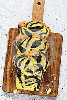 Unusual pumpkin marbled tiger print bread with cuttlefish ink, braided on a wooden board on a light background.