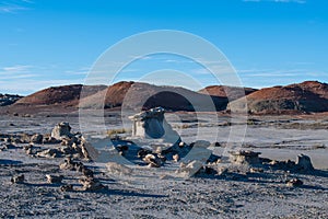 Unusual rock formations in a desert landscape with a background of orange and red hills at Bisti Badlands in New Mexico