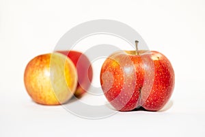 Unusual shape of bright ripe red apple in the shape of an ass in the light of the sun on a white background with two usual apples