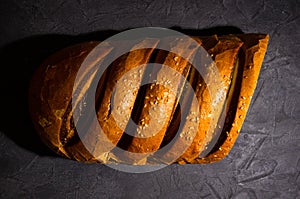 Unusual two-color fresh loaf of bread on a black background, photo in a low key in hard light, close-up.