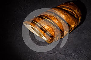 Unusual two-color fresh loaf of bread on a black background, photo in a low key in hard light, close-up.