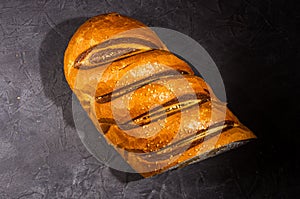 Unusual two-color fresh loaf of bread on a black background, photo in a low key in hard light, close-up.