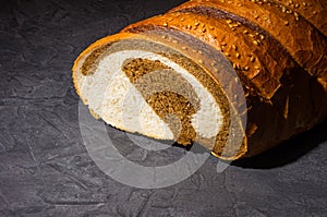 Unusual two-color fresh loaf of bread on a black background, photo in a low key in hard light, close-up.