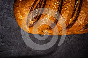 Unusual two-color fresh loaf of bread on a black background, photo in a low key in hard light, close-up.