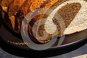 Unusual two-color fresh loaf of bread in a ceramic plate and a woven napkin on a black background, photo in a low key in
