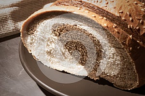 Unusual two-color fresh loaf of bread in a ceramic plate and a woven napkin on a black background, photo in a low key in