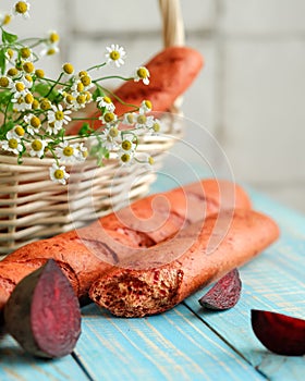 Unusual vegetable bread with beetroot. Broken loaf of bread on rustic table with basket of daisies on blurred background