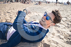 Unusual young man in elegant suit relaxes on the beach and laughs