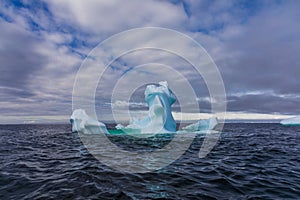 An unusually shaped iceberg floats in the sea against a blue and cloudy sky, Antarctica