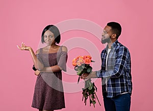 Unwanted confession. Displeased black woman rejecting her admirer with roses on Valentine's Day over pink background