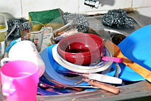 Unwashed kitchen utensils in the wash basin need to be cleaned and washed, a pile of dirty dishes, knives, pots and drinking glass