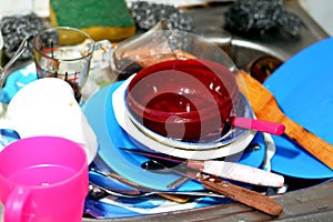 Unwashed kitchen utensils in the wash basin need to be cleaned and washed, a pile of dirty dishes, knives, pots and drinking glass