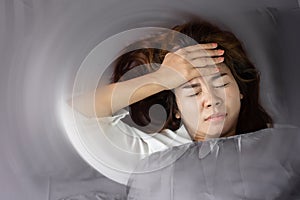 Unwell Asian woman having headache , migraine or vertigo  lying in bed with hand holding her head photo