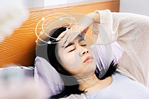 Unwell Asian woman suffering from dizziness after wakeup in morning hand holding her head lying down in bed