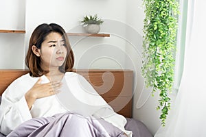 Unwell Asian woman suffering from nausea, sore throat ,morning sick sitting in bed