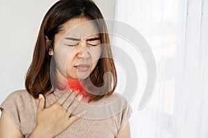 Unwell Asian woman suffering from sore throat, heartburn hand holding her painful neck