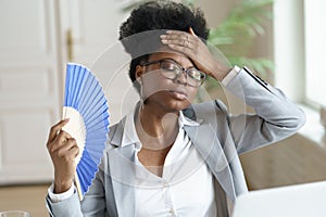 Unwell black business woman hold waver feel sick, hot and overheated work on computer at home office