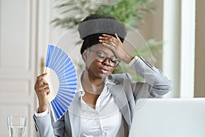 Unwell black business woman hold waver feel sick, hot and overheated work on computer at home office