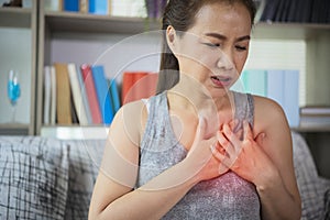 Unwell condition and sickness concept; Asian woman having heart attack sitting on sofa