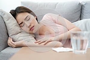 Unwell condition young Asian girl sleeping on sofa after checking temperature and taking medicines and water, Health and illness