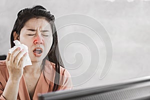 Unwell female Asian having flu and cold sneezing at work place photo