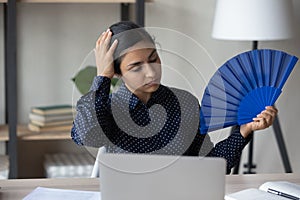 Unwell Indian woman wave with hand fan at workplace